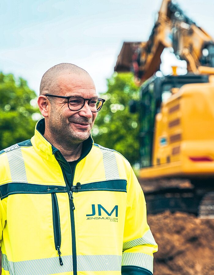 Mitarbeiter eines Tiefbauunternehmens vor einem Bagger auf der Baustelle