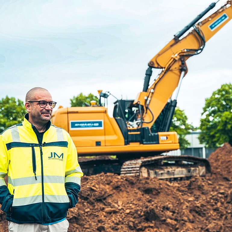 Mitarbeiter auf einer Erd- und Tiefbaustelle vor einem Kettenbagger